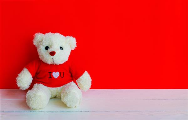 عروسک خرس روی میز تخته ای چوبی با زمینه رنگ صورتی قرمز مفهوم ولنتاین
