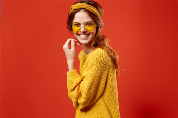 زن پس زمینه قرمز در تزئین عینک آفتابی ژاکت زرد روی مو