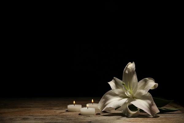زنبق زیبا و شمع های سوزان در پس زمینه تیره با فضایی برای متن گل تشییع جنازه