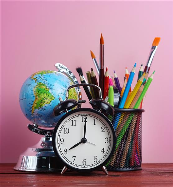 جهان گلوب ساعت زنگ دار و ثابت مدرسه در سبد روی میز چوبی صورتی رنگ