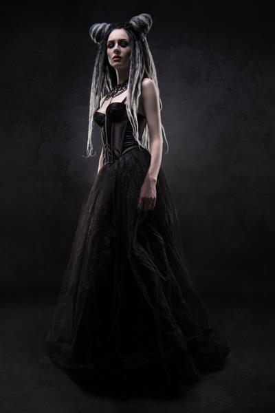 زنی با ترس و لباس گوتیک سیاه که روی پس زمینه تیره ژست گرفته است
