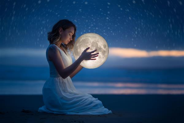 عکاسی ظریف طالع بینی جادوی زنانه دختر زیبا و جذاب در ساحل شبانه با شن و ماسه و ستاره ماه را در آغوش می گیرد عکاسی هنری