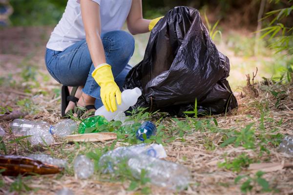 دست زن جوان آسیایی در حال برداشتن پلاستیک زباله برای تمیز کردن در پارک حفاظت از محیط زیست