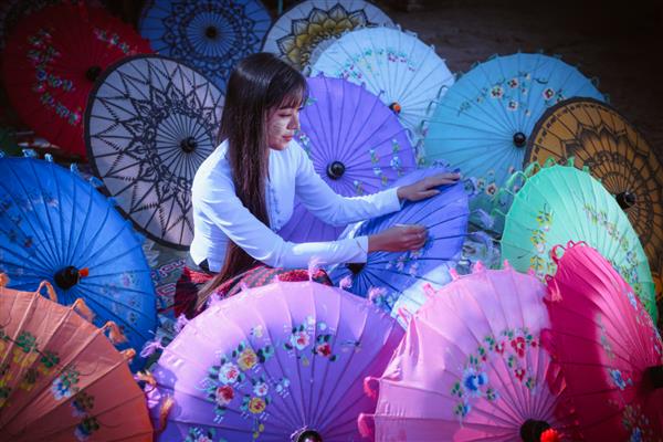 یک زن مدل آسیایی زیبا با لباس های سنتی لبخند ژست نقاشی چتر دست ساز با پس زمینه چتر رنگارنگ