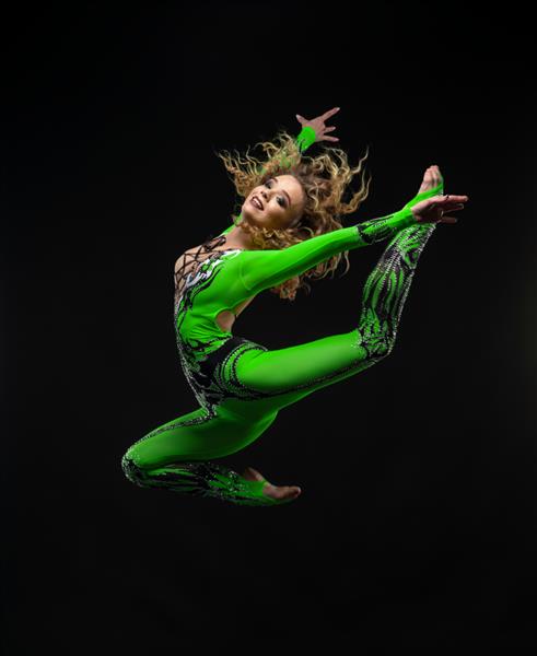 زن ورزشکار زیبا با مدل موی مجعد در لباس سبز رنگ که روی پس زمینه تیره می پرد