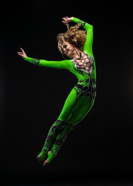 زن ورزشکار زیبا با مدل موی مجعد در لباس سبز رنگ که روی پس زمینه تیره می پرد