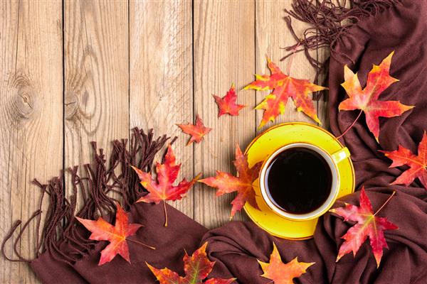 فنجان قهوه سیاه روسری نساجی قهوه‌ای میز چوبی با برگ‌های نارنجی پاییزی قرمز زرد و صاف نمای بالا ماکت‌آپ سلام سپتامبر اکتبر نوامبر مفهوم فصلی
