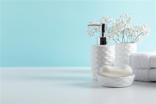 دکور ملایم حمام به رنگ سفید حوله دستگاه پخش صابون گل های سفید لوازم جانبی روی قفسه آبی پاستلی دکوراسیون داخلی حمام زیبا