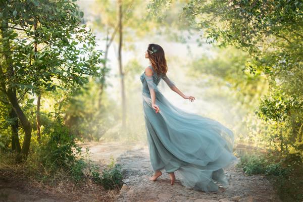 شاهزاده خانم افسانه ای با لباس آبی فیروزه ای روشن تابستانی در مسیری وسیع و به سمت باد می رود دختر رقصنده برازنده در تصویر گل با لبه بلند لباس پرنده پوره جنگل سبز روشن