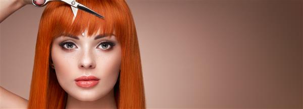 زن جوان زیبا با آرایشی روشن و موهای بلند صاف قیچی فلزی در دست دارد مدل موهای قرمز آرایشگاه مدل مو محصولات مراقبت و زیبایی مو آرایش کامل