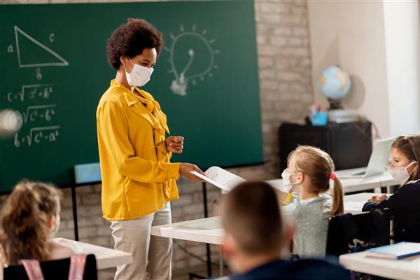 معلم سیاه پوست شاد و دانش آموزانش که ماسک محافظ صورت در کلاس درس می پوشند معلم نتایج آزمون خود را به آنها می دهد
