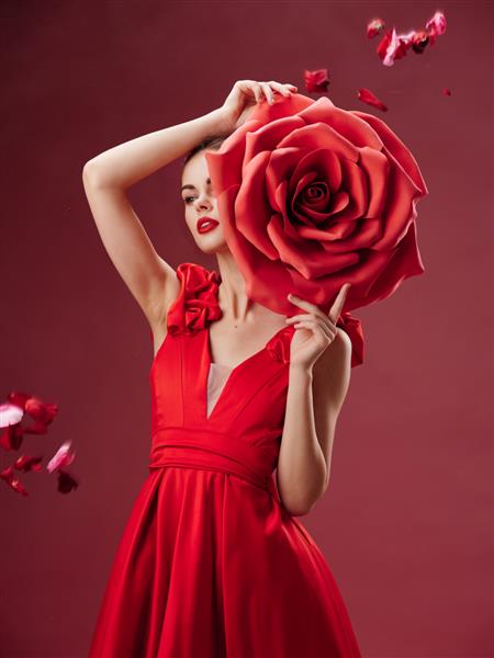 لباس قرمز زن مجلل که یک گل رز بزرگ در دستانش گلبرگ های در حال افتادن نگه داشته است
