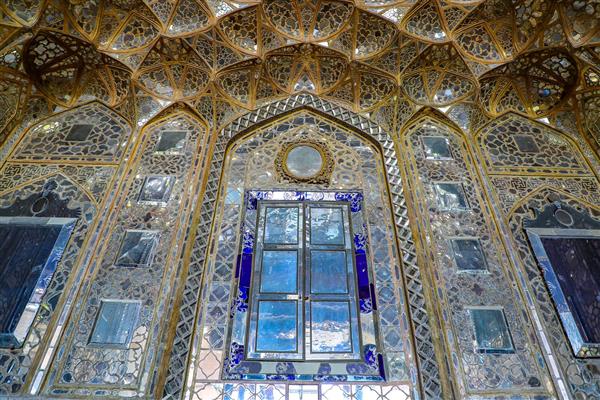 عکس پنجره چوبی مشبک با شیشه‌های آبی در میان تزئینات آینه‌کاری عالی قاپو