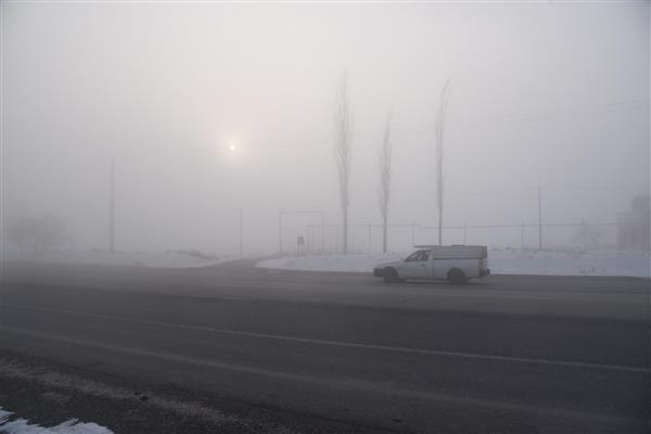 خودرو ون سفید در حال عبور از جاده مه‌آلود کنار خطوط در زمستان