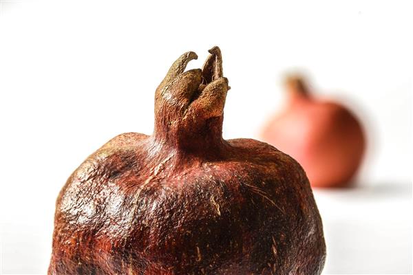 کلوزآپ میوه انار چروکیده و خشک با تمرکز بر تاج روی پس‌زمینه سفید