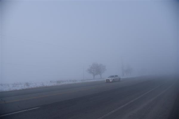 خودرو سواری در حال حرکت در جاده غرق در مه و برف در طول روز