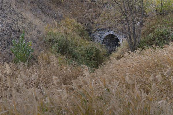 دروازه تونل سنگی قدیمی در دل پوشش گیاهی و علفزارهای خشک پاییزی