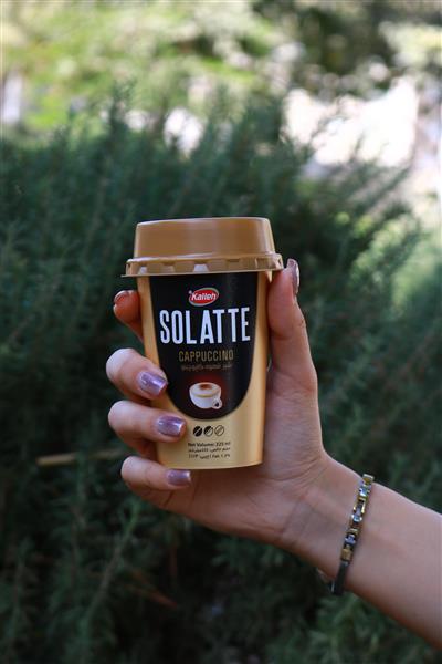 دست زن با لاک بنفش در حال نگه‌داشتن لیوان آماده کاپوچینو در فضای سبز