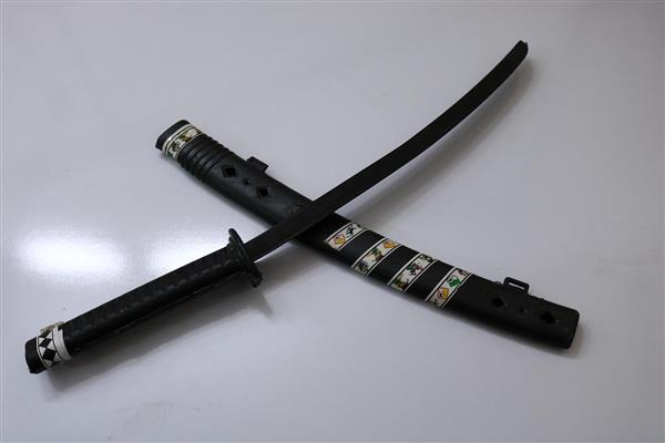 عکس استودیویی از شمشیر کاتانا ژاپنی مشکی با غلاف و دسته تزئین شده روی زمینه سفید