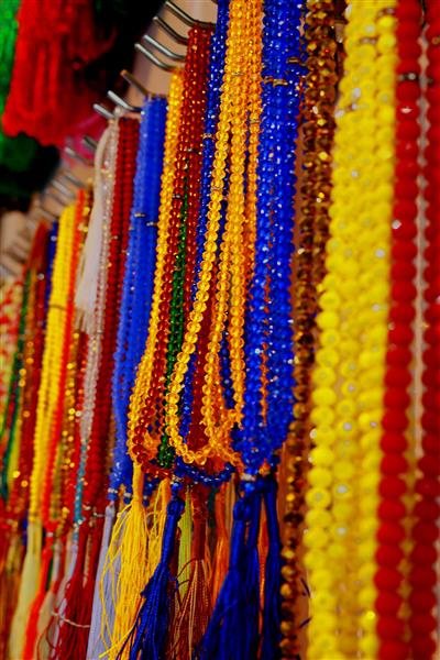 نمای نزدیک از آویزها و تسبیح‌های کریستالی و مهره‌ای رنگارنگ برای دکور و فروش