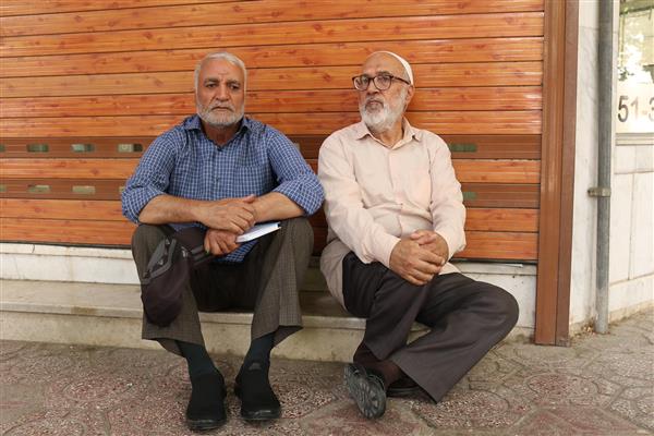 پرتره دو پیرمرد ایرانی با کلاه و ریش در حال استراحت و گپ زدن کنار درب مغازه