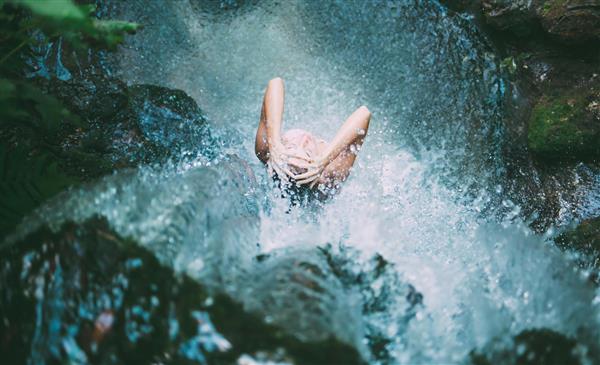 عکس باکیفیت طبیعت و فردی در زیر آبشار کوهستانی برای پوستر دیواری سالن‌های ورزشی، استخر، حمام‌های لوکس و لابی