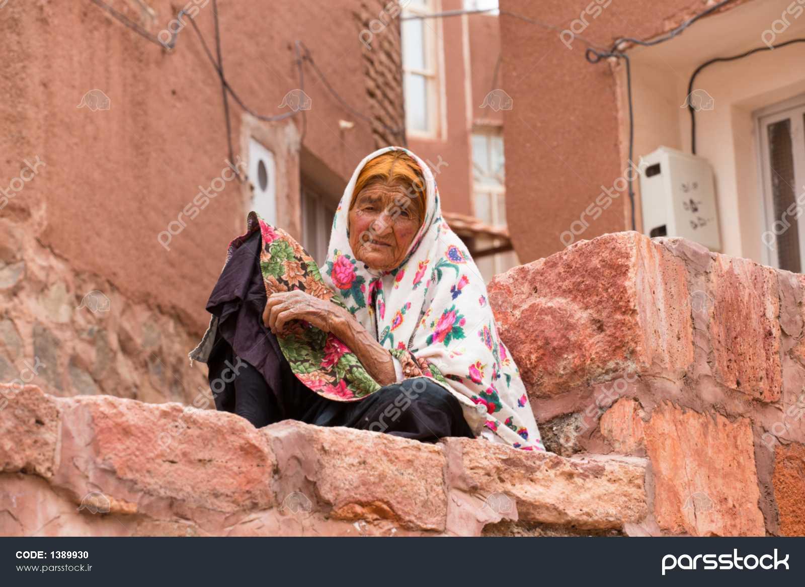 کاشان ایران 2015 مه 2 یک زن سالخورده در روستای باستانی آبیانه در نزدیکی  کاشان در ایران است در پس زمینه خانه های آجری قرمز آبیانه 1389930