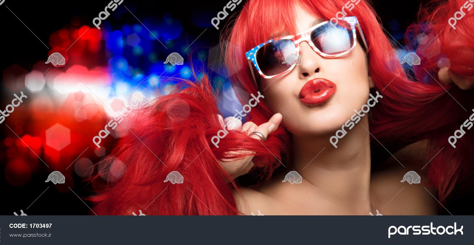 زن زیبای سکسی با موهای قرمز بلند با عینک آفتابی پرچم آمریکا چهارم ژوئیه را  جشن می گیرد و لب های پرپشت خود را در یک حرکت حسی به دوربین می زند