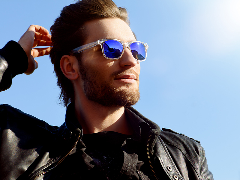 Confident handsome man in sunglasses and leather jacket over blue sky Men