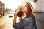 پرتره سبک زندگی خندان تابستانی در فضای باز از زن جوان زیبا در حال تفریح در شهر در اروپا در عصر با دوربین عکاسی عکاسی که با عینک و کلاه سبک هیپستر عکس می گیرد