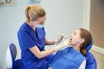 مفهوم مردم پزشکی دهان شناسی و مراقبت های بهداشتی - دندانپزشک زن شاد با آینه در حال بررسی دندان های دختر بیمار در مطب کلینیک دندانپزشکی