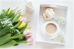 صبحانه صبح در بهار با یک فنجان قهوه سیاه با شیر و شیرینی به رنگ های پاستلی یک دسته گل لاله تازه زرد و صورتی در زمینه سفید نمای بالا