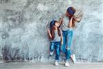 مامان جوان زیبا با دخترش با پوشیدن تی شرت خاکستری خالی و شلوار جین در مقابل دیوار بتنی خشن سبک مد خیابانی مینیمالیستی ظاهر خانواده لباس برای والدین و فرزند