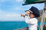 کاپیتان کوچک بامزه در قایق بادبانی در حال تماشای دریای دریایی در سفر تابستانی ماجراجویی سفر قایق سواری با کودک در تعطیلات خانوادگی لباس بچه گانه در سبک ملوانی مد دریایی