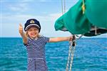 کاپیتان بچه کوچک خوشحال در قایق بادبانی در حال تماشای دریای دریایی در سفر تابستانی ماجراجویی سفر قایق سواری با کودک در تعطیلات خانوادگی لباس بچه گانه در سبک ملوانی مد دریایی
