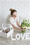 گلفروش دسته گل را در مغازه نمایش می دهد پیشنهاد دختر جوان برای خرید یک دسته گل سفید عروس در یک کارگاه استودیو دکوراتور سبک با دیوار آجری در پس‌زمینه