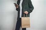 دختر جوان هپستر با استفاده از تلفن های هوشمند مدرن و برگزاری سفارشی خرید کیسه های خرید مدل بسته کاغذ قهوه ای مفهوم خرید آنلاین