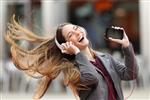 دختر با هیجان و گوش دادن با هدفون و گوشی هوشمند در خیابان با حرکت موها