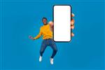 مرد سیاهپوست میانسال خوش تیپ احساسی با لباس گاه به گاه شیک در حال پریدن با تلفن همراه مدرن با صفحه سفید خالی نمایش برنامه زیبا روی پس زمینه آبی استودیو ماکت فضای کپی